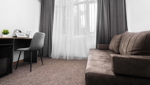 A hotel room with a desk, chair, and sofa.