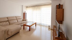 Ein Wohnzimmer mit einem beigefarbenen Sofa, einem Holztisch und einem Fernseher auf einem Holzgestell.
