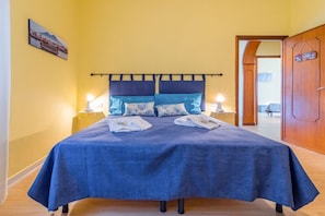 A bed with a blue bedspread, two pillows, two bedside lamps, and a wooden door in the background.