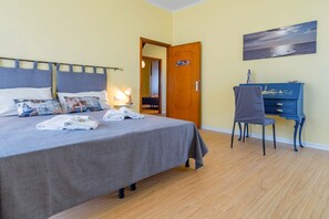 A bedroom with a bed, bedside table, lamp, chair, dresser, and a door leading to another room.