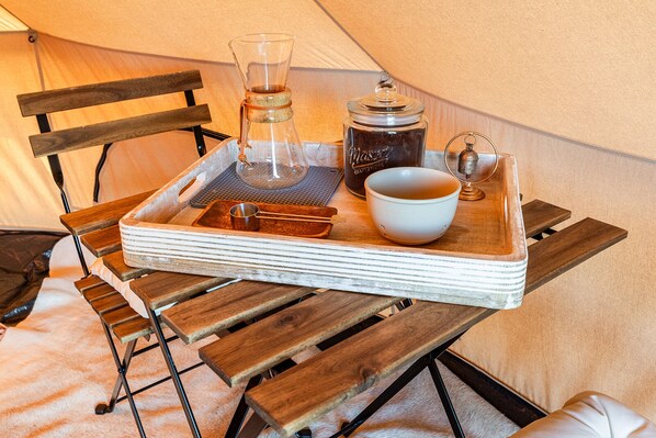 A wooden table with a tray holding a glass carafe, a metal cup, a ceramic mug, and a small container. - Glamping Tibet Tent #1 (Whitehall)