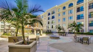 Un patio con una palmera, asientos al aire libre y un edificio con varios balcones.