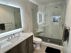 Une salle de bain moderne avec une douche à parois de verre, un grand miroir et un comptoir en marbre.