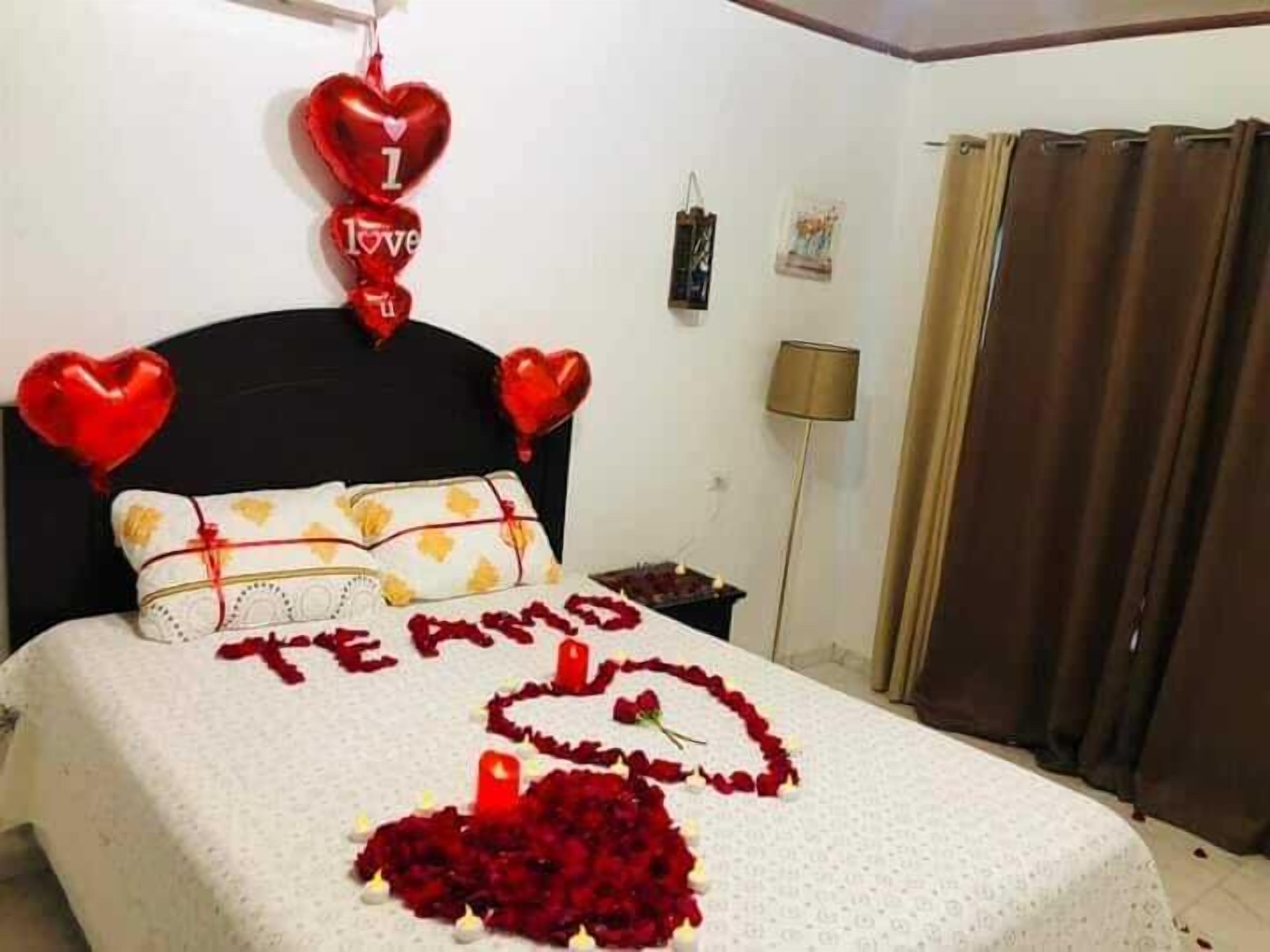 Un dormitorio con cama, adornos con forma de corazón y un arreglo de globos que dice 'Te amo'.