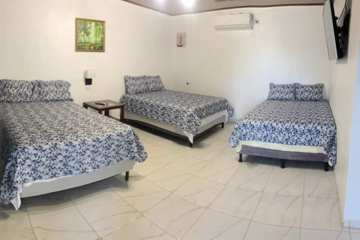 Een kamer met drie bedden, elk voorzien van een bloemenprint sprei, een klein nachtkastje en een wandgemonteerde airconditioning.
