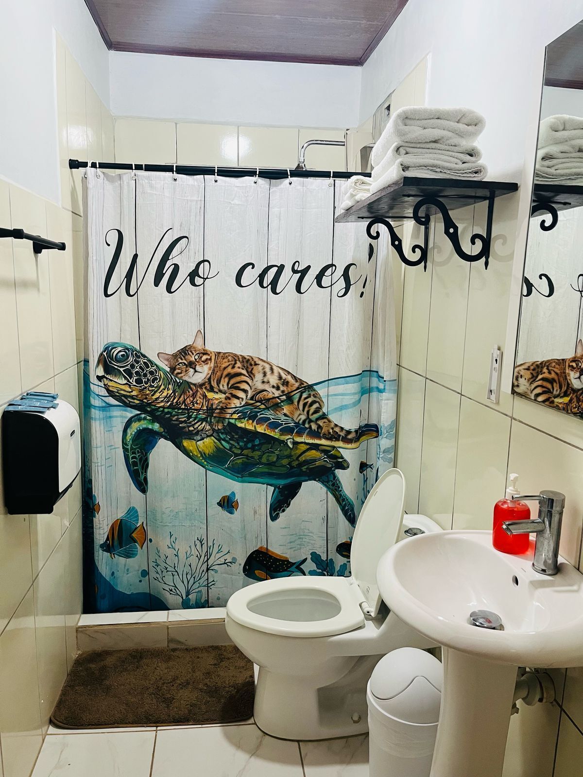 Un baño con inodoro, lavamanos y cortina de ducha con un gato y una tortuga.