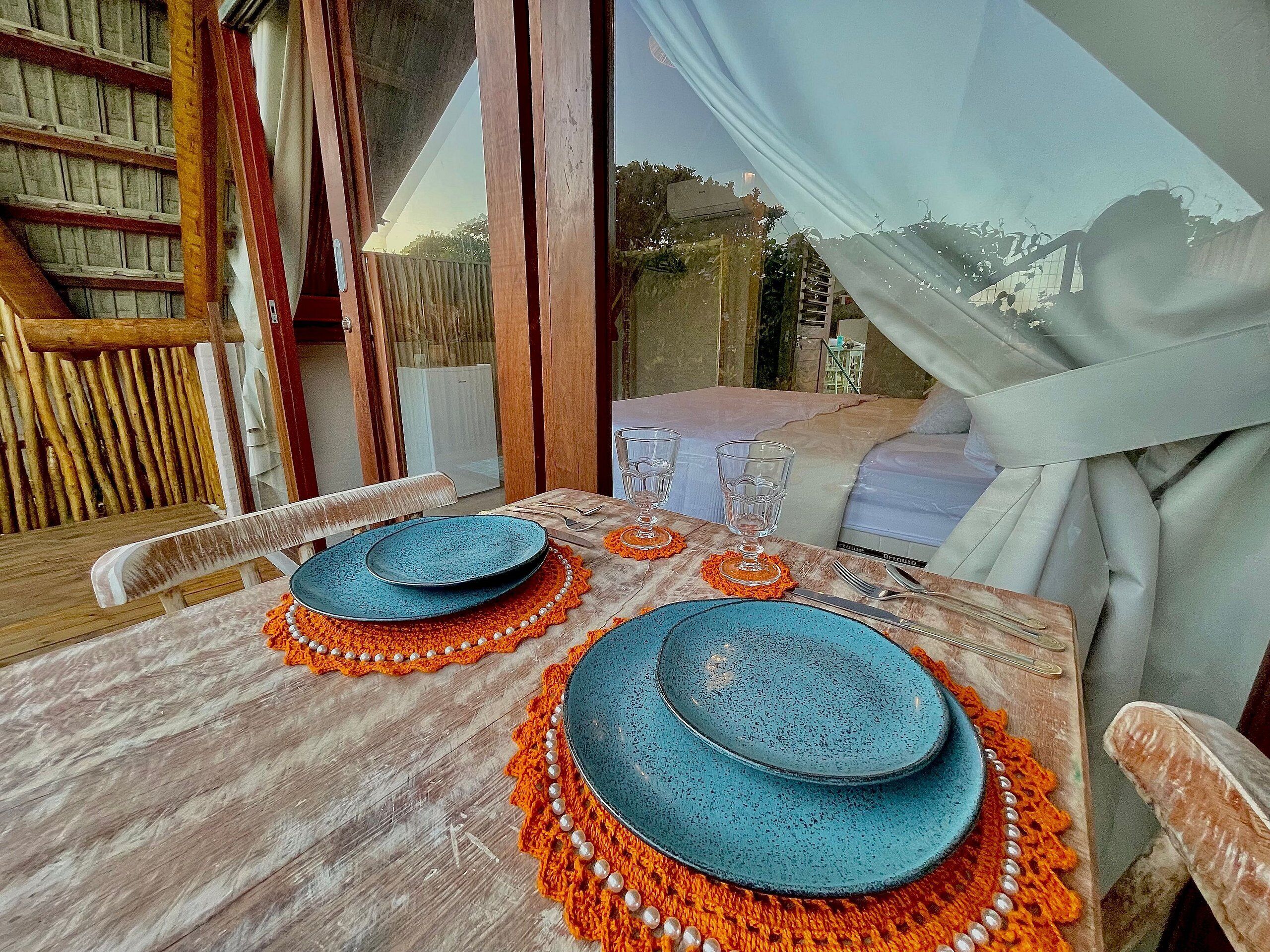 A dining table set with blue plates, orange placemats, and clear glassware.