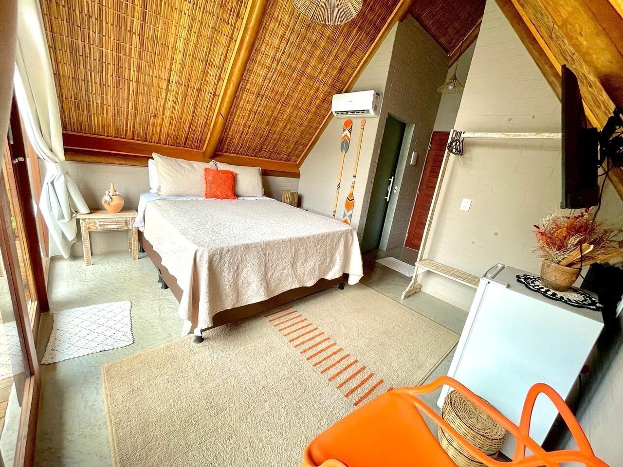 A bedroom with a bed, a small table, a chair, and a refrigerator.