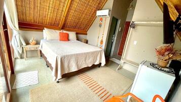 A bedroom with a bed, a small table, a chair, and a refrigerator.
