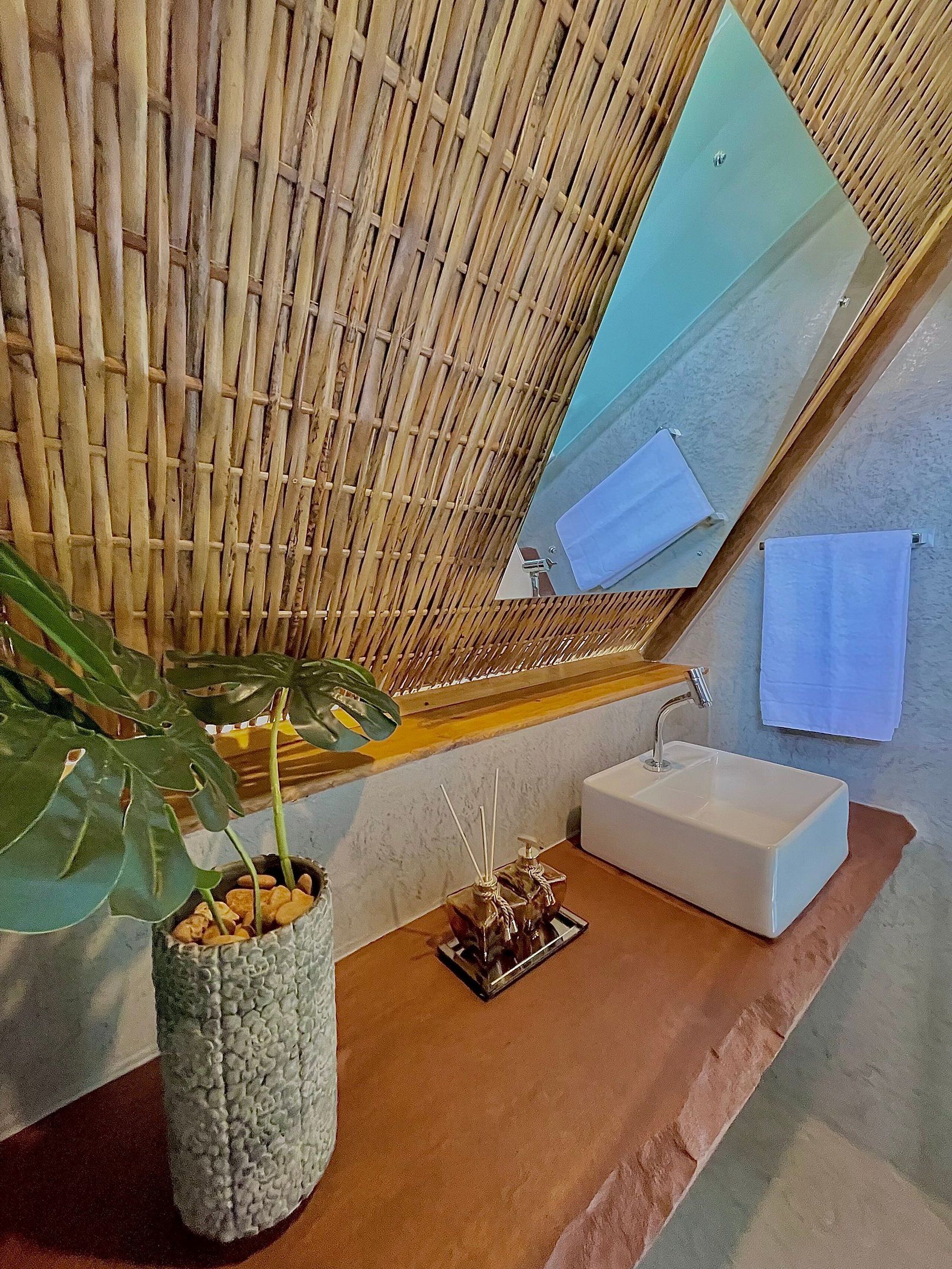 A bathroom with a bamboo wall, a large mirror, a sink, and a potted plant.