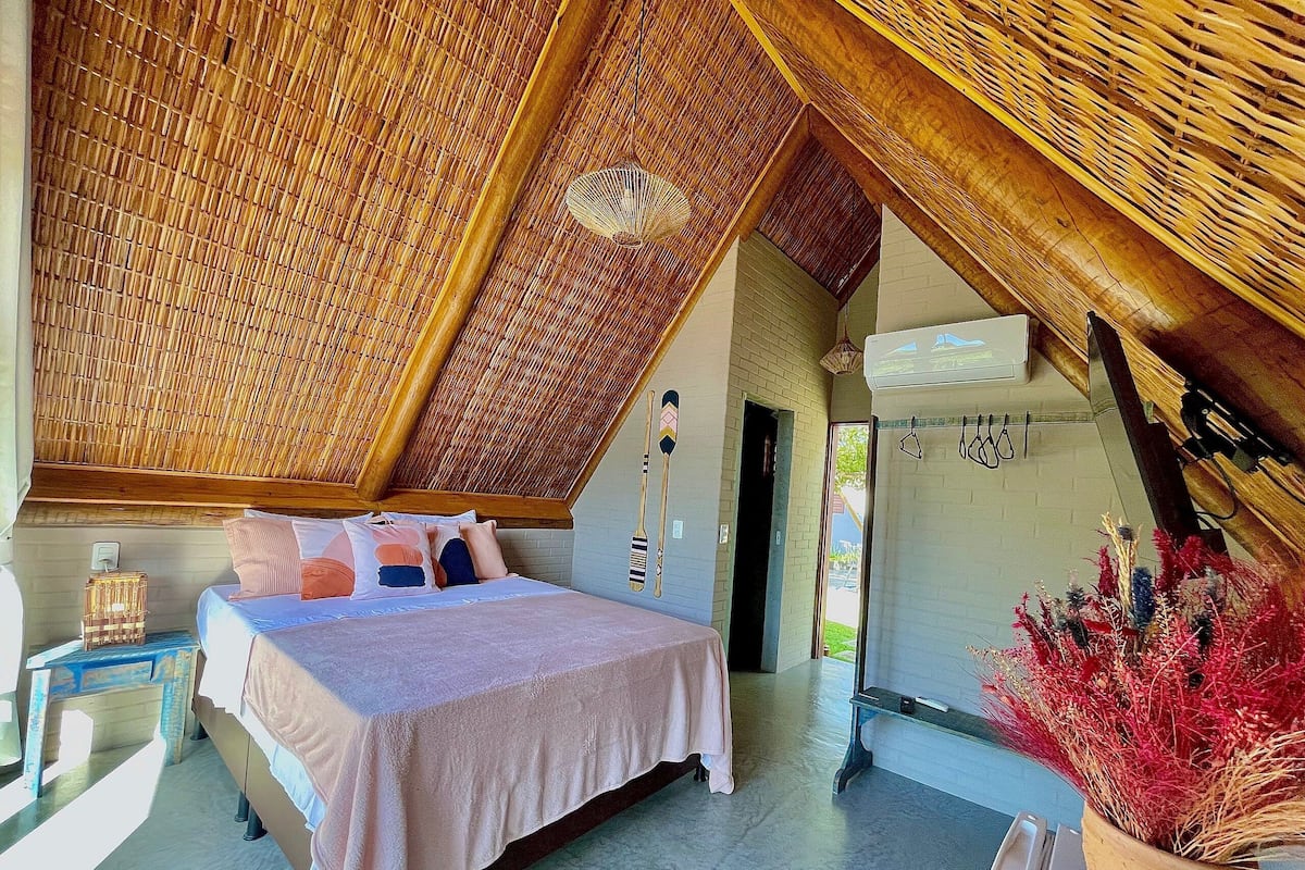 A bedroom with a bed, a nightstand, a potted plant, and a wall-mounted fan.