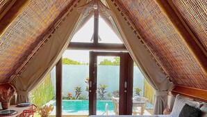 Un dormitorio con una cama grande, vista a una piscina y un techo alto e inclinado.