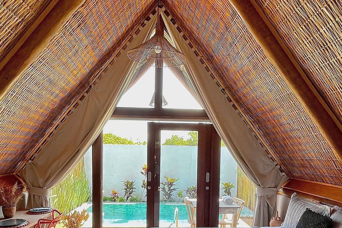 A bedroom with a large bed, a view of a swimming pool, and a high, sloped ceiling.