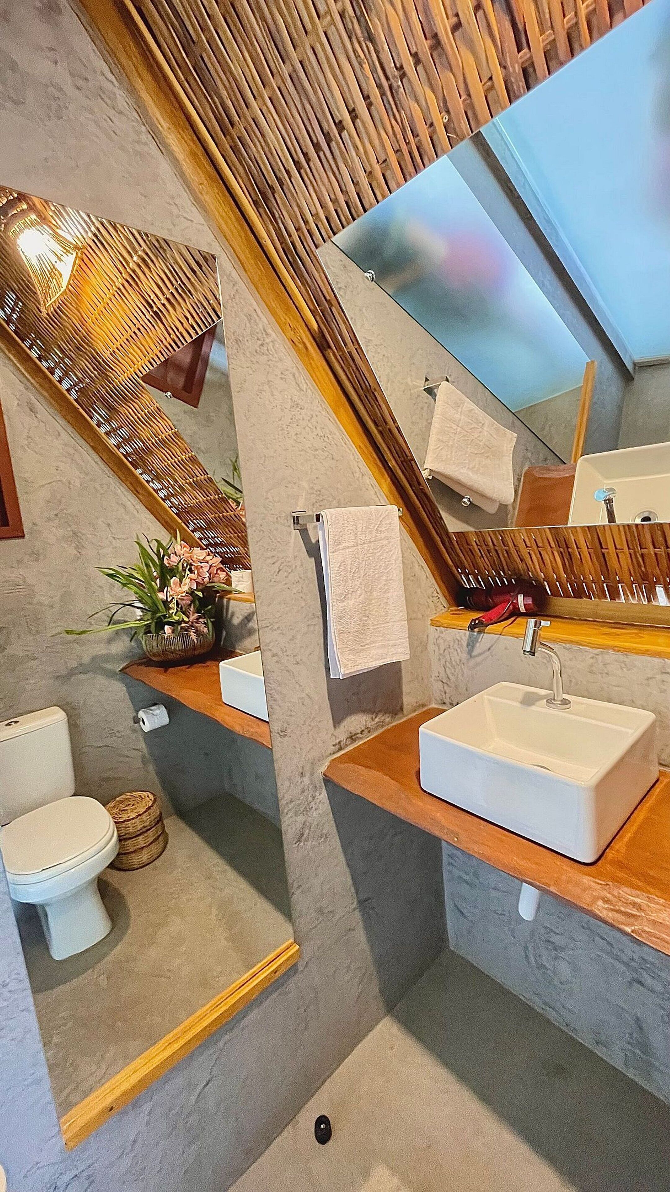 Et moderne badeværelse med træloft, et stort spejl, en hvid vask og et toilet.