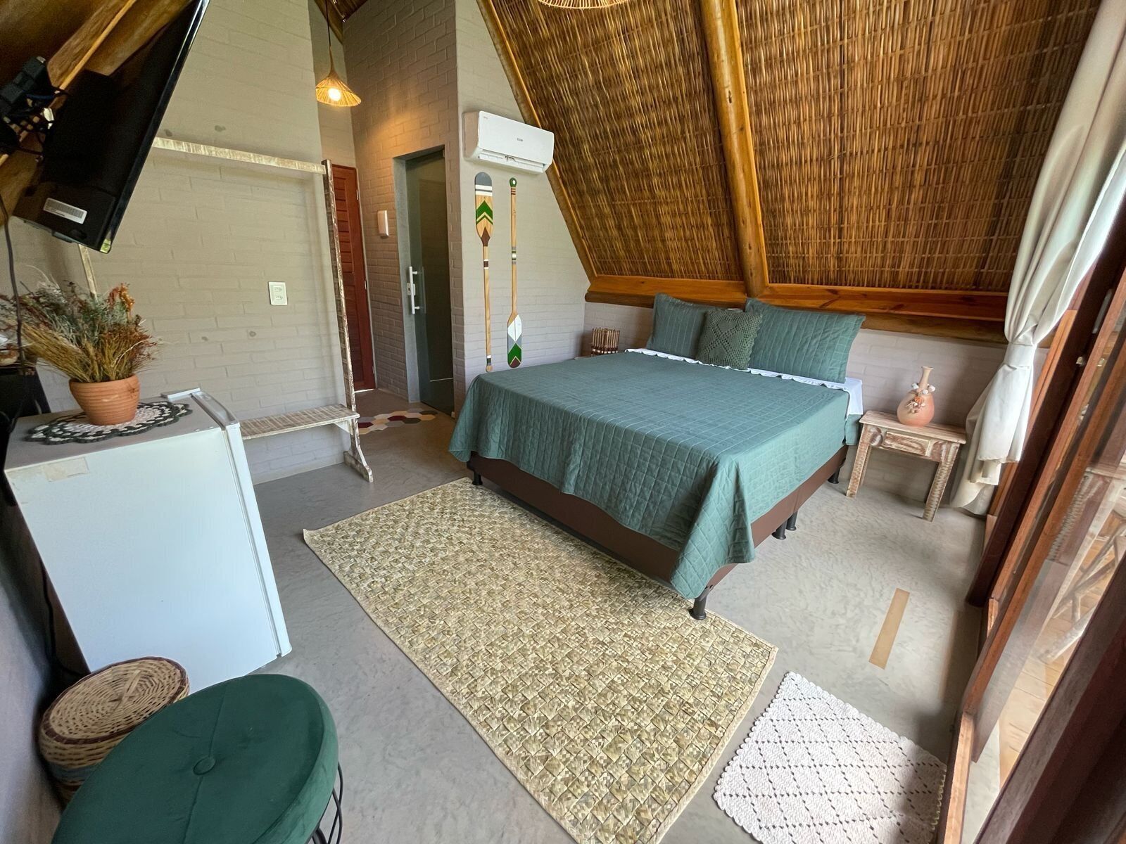A cozy, rustic bedroom with a sloped ceiling, a bed with green bedding, a small table, and a refrigerator.