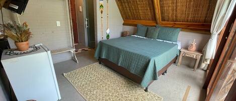 A cozy, rustic bedroom with a sloped ceiling, a bed with green bedding, a small table, and a refrigerator.