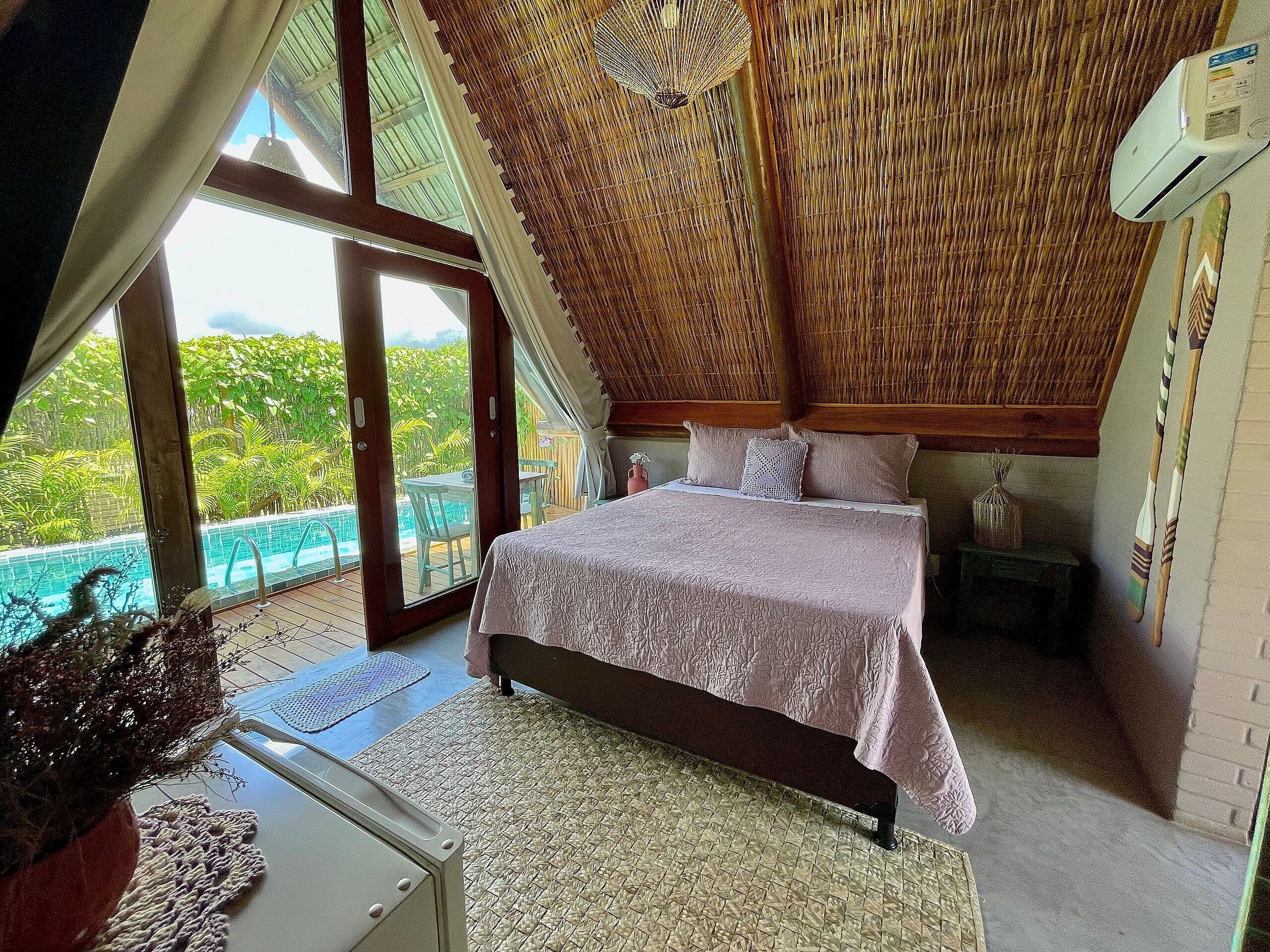 A bedroom with a large bed, a view of a swimming pool, and a high ceiling with a woven design.