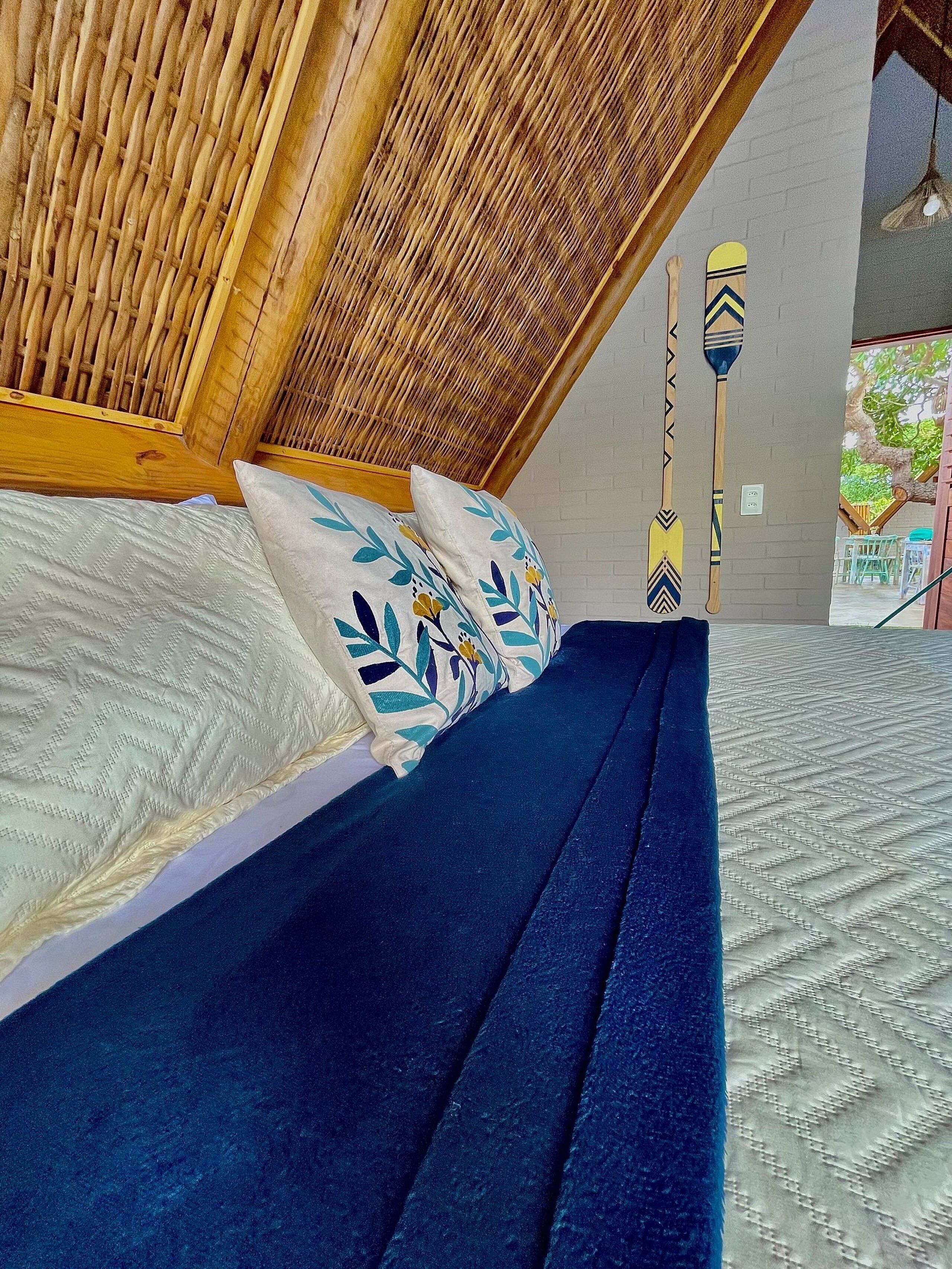 Ein Bett mit blauem Kopfteil, weißen Kissen mit Blattmotiven und einer strukturierten, weißen Bettdecke.