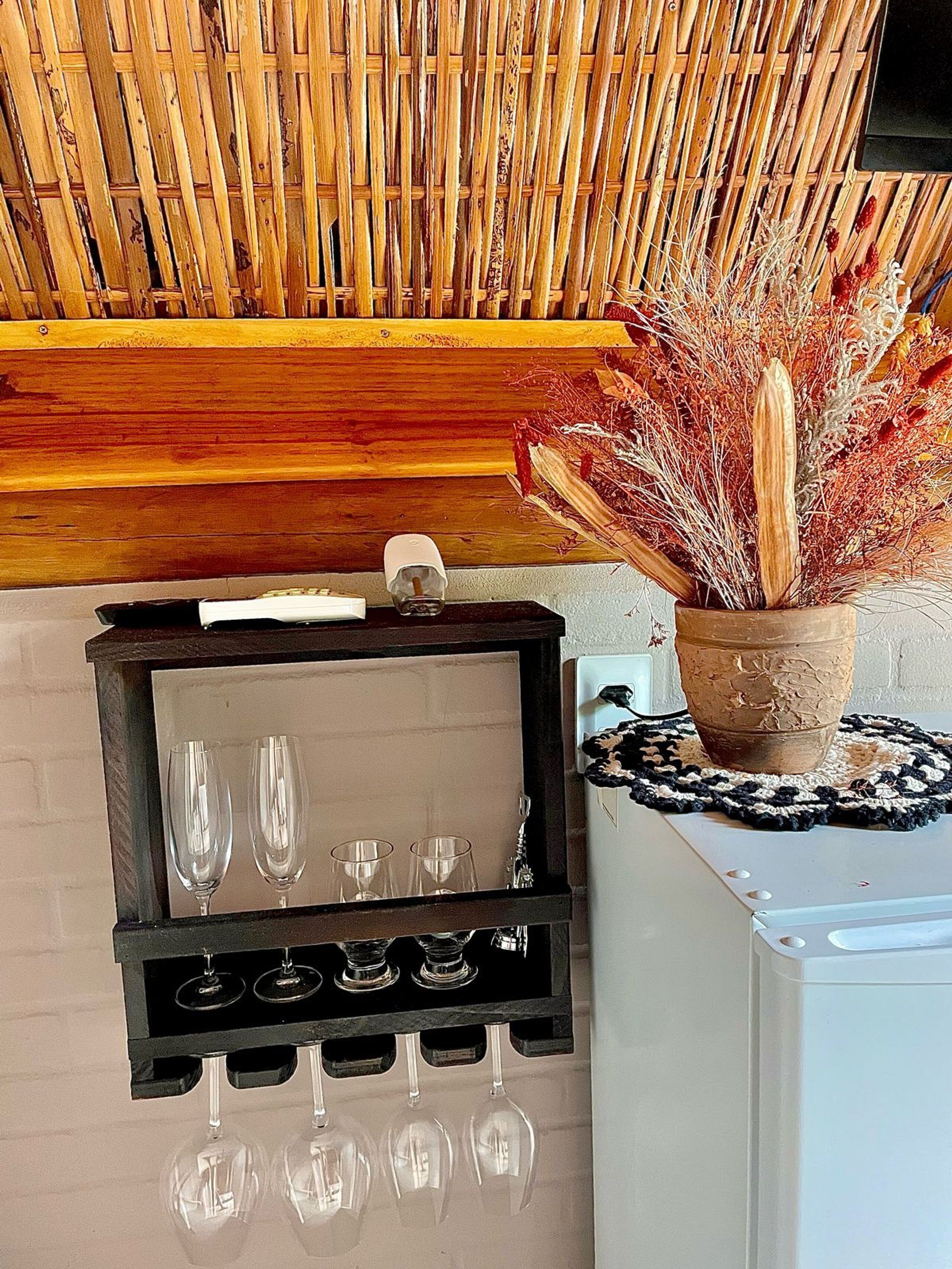 A wine rack with six glasses, a potted plant with dried flowers, and a wooden wall.