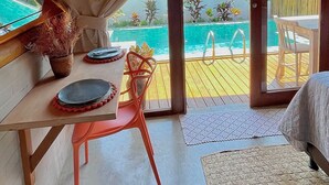 Una habitación con un amplio ventanal con vista a una piscina, un comedor con mesa y sillas, y una cama orientada a la piscina.