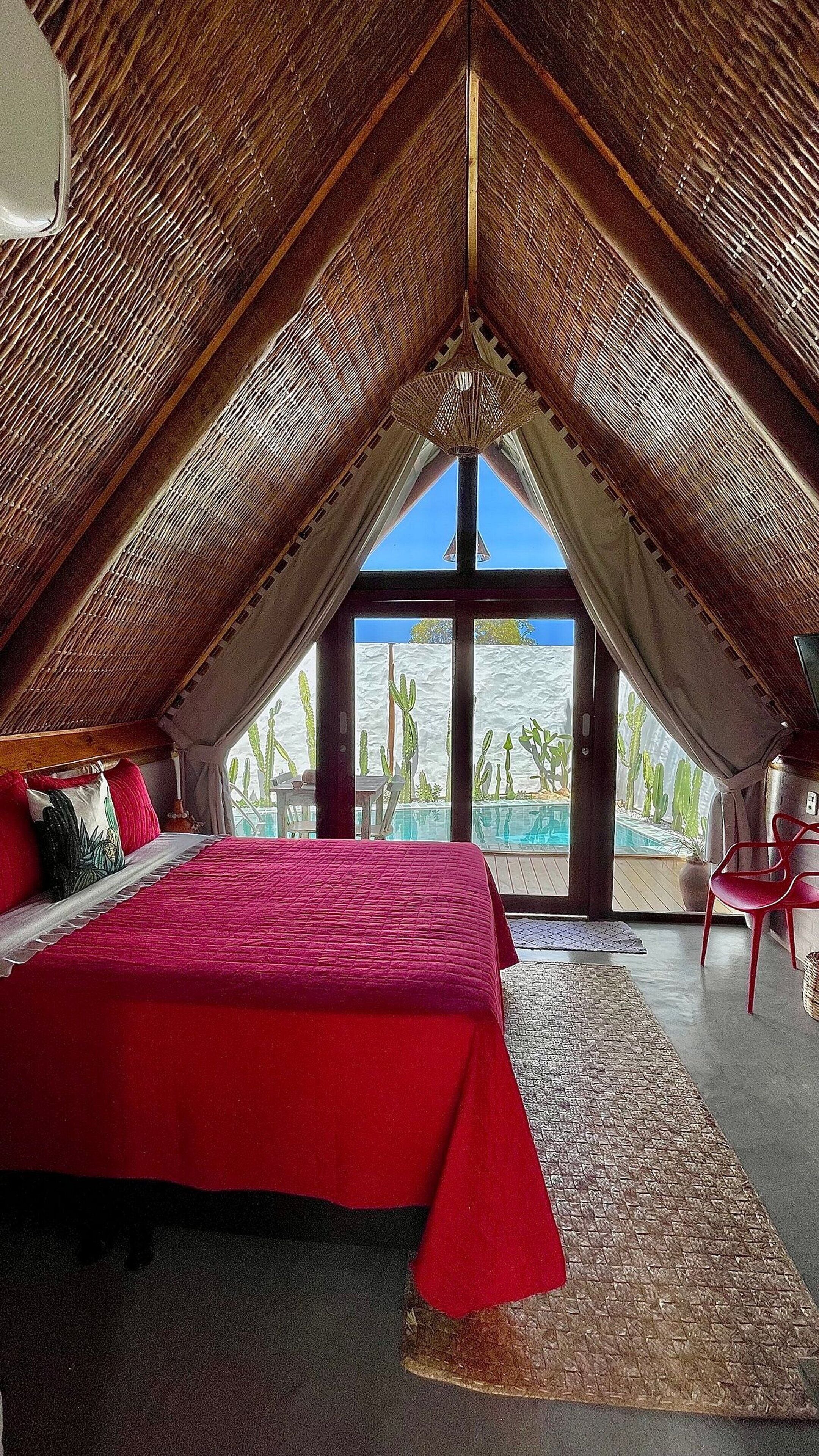 A bedroom with a large bed, a view of a pool, and a cactus garden outside.