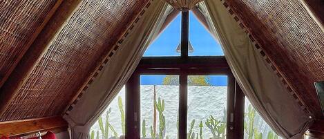 A bedroom with a large bed, a view of a pool, and a cactus garden outside.