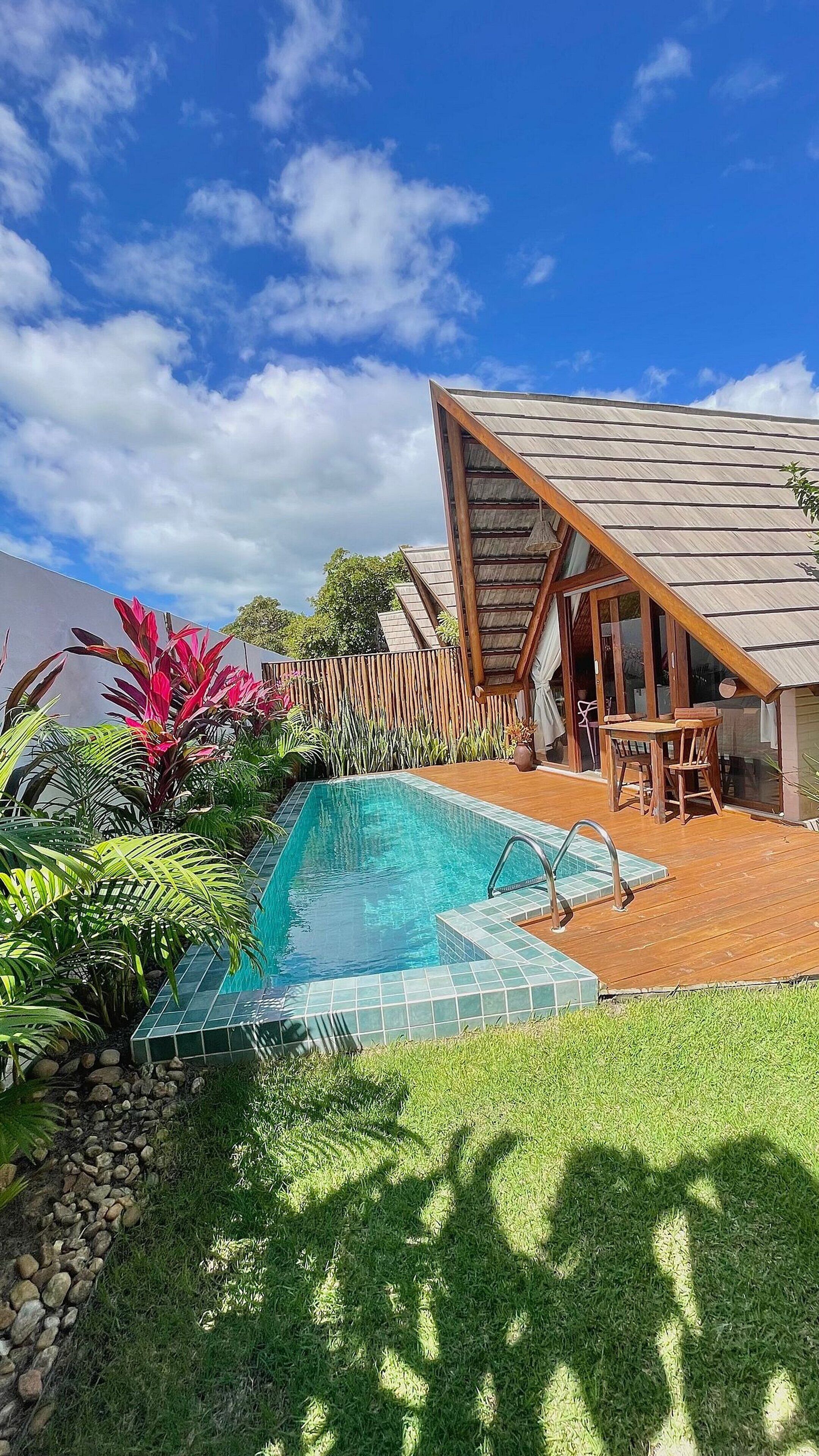 Una piscina con terraza de madera y zona de estar cubierta.