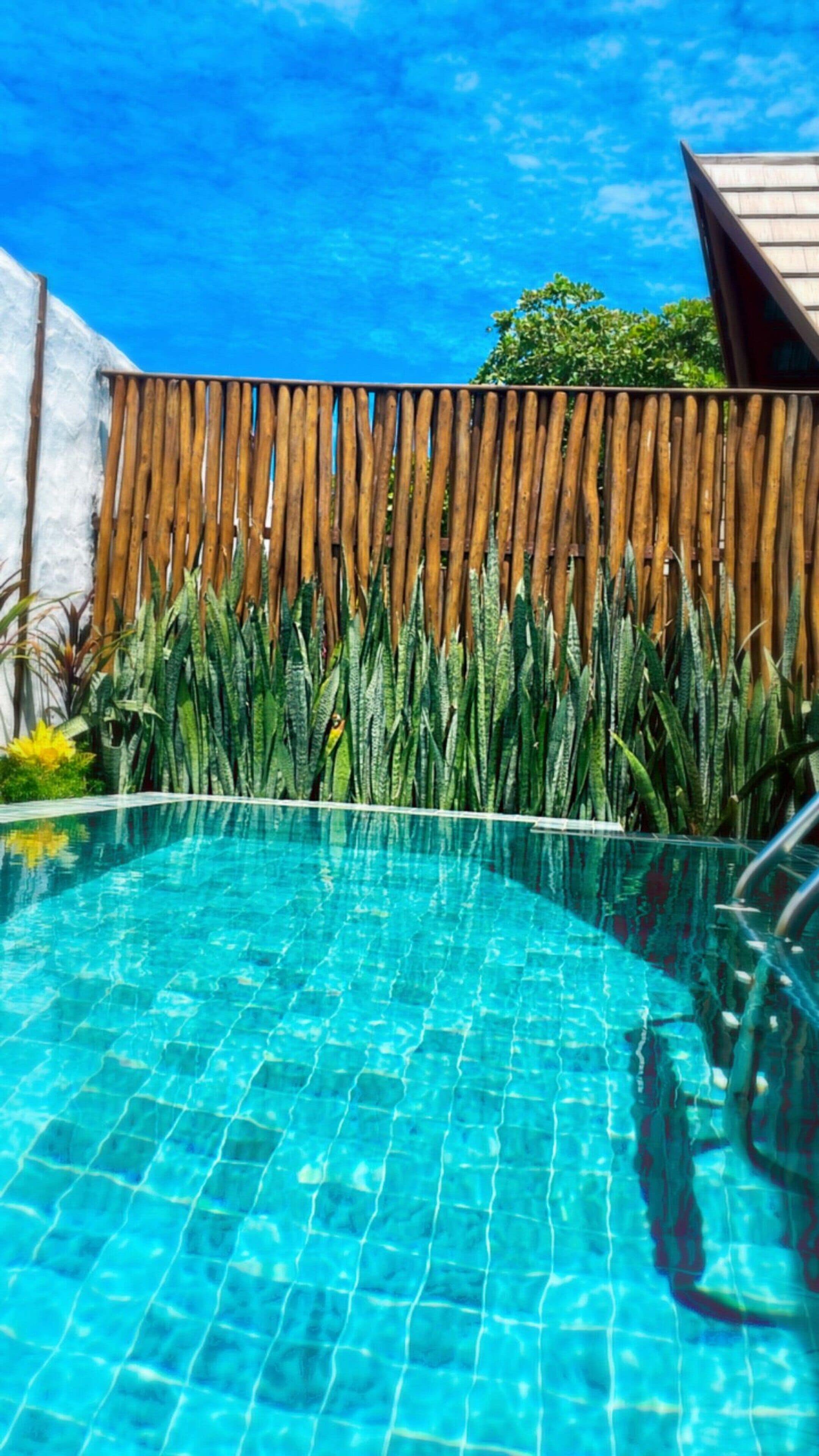 Una piscina azul cristalina con una cerca de madera y plantas verdes al fondo.