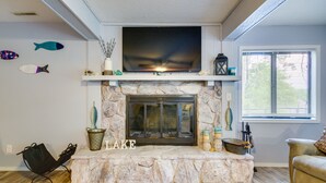 A living room with a stone fireplace, a flat-screen TV mounted above it, and decorative fish on the wall. - Waterfront Home w/ Views & Dock in Sunrise Beach! (Sunrise Beach)