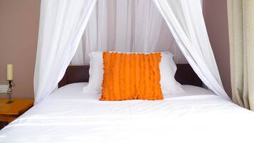 Una cama con ropa de cama blanca, un almohador naranja y un dosel blanco.