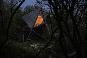 A triangular treehouse with a visible interior, surrounded by dense forest.