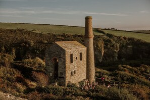 A stone building with a chimney, surrounded by greenery and a clear sky.