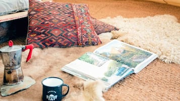 A cozy room with a patterned pillow, a coffee pot, a mug, and a magazine on a fluffy carpet.