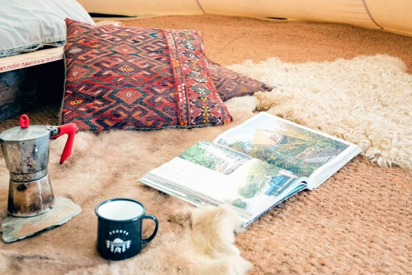Une pièce chaleureuse avec un coussin à motifs, une cafetière, une tasse et un magazine posés sur un tapis moelleux.