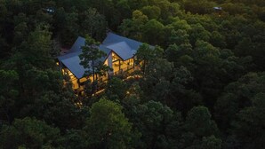 Une maison entourée d’une forêt dense, dotée d’un balcon bien visible et d’une grande fenêtre.
