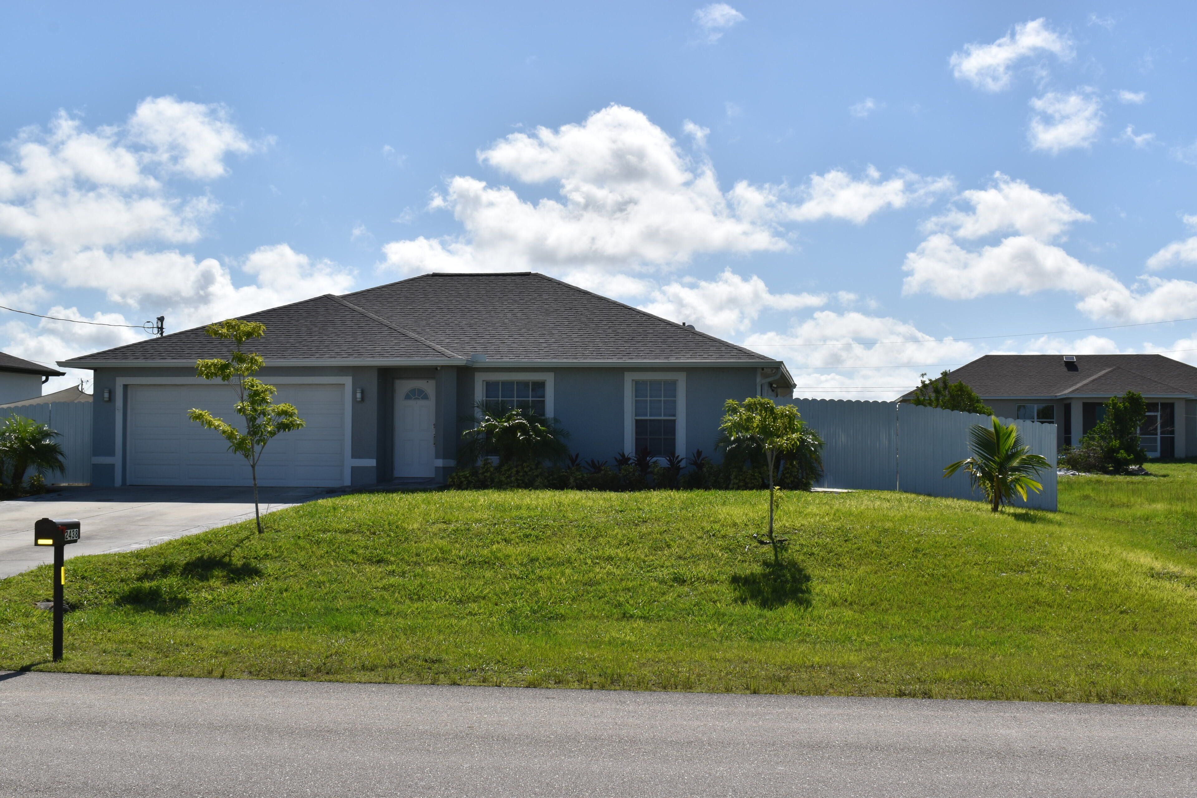 A residential house with a sloped roof, a garage, and a well-maintained lawn with small trees.
