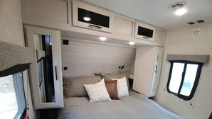 A bedroom with a bed, pillows, a mounted TV bracket, and a window. - Country RV Glamping with lake, mountain and orchard views! (Chelan)