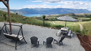 A patio with a swing set, three Adirondack chairs, a grill, and a striped umbrella. - Country RV Glamping with lake, mountain and orchard views! (Chelan)