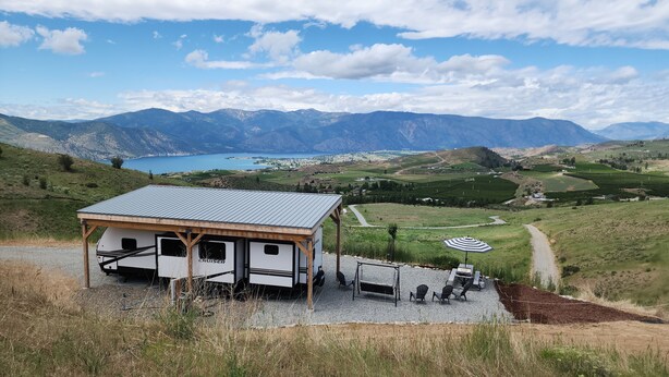 A cabin with a metal roof and wooden beams, a gravel driveway, and a scenic view of mountains and a lake. - Country RV Glamping with lake, mountain and orchard views! (Chelan)