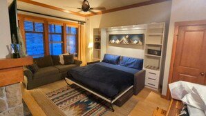 A bedroom with a bed, a sofa, a fireplace, a ceiling fan, and built-in shelving. - Beautiful End-Unit with Private Balcony and hot tub + pool. (Solitude)