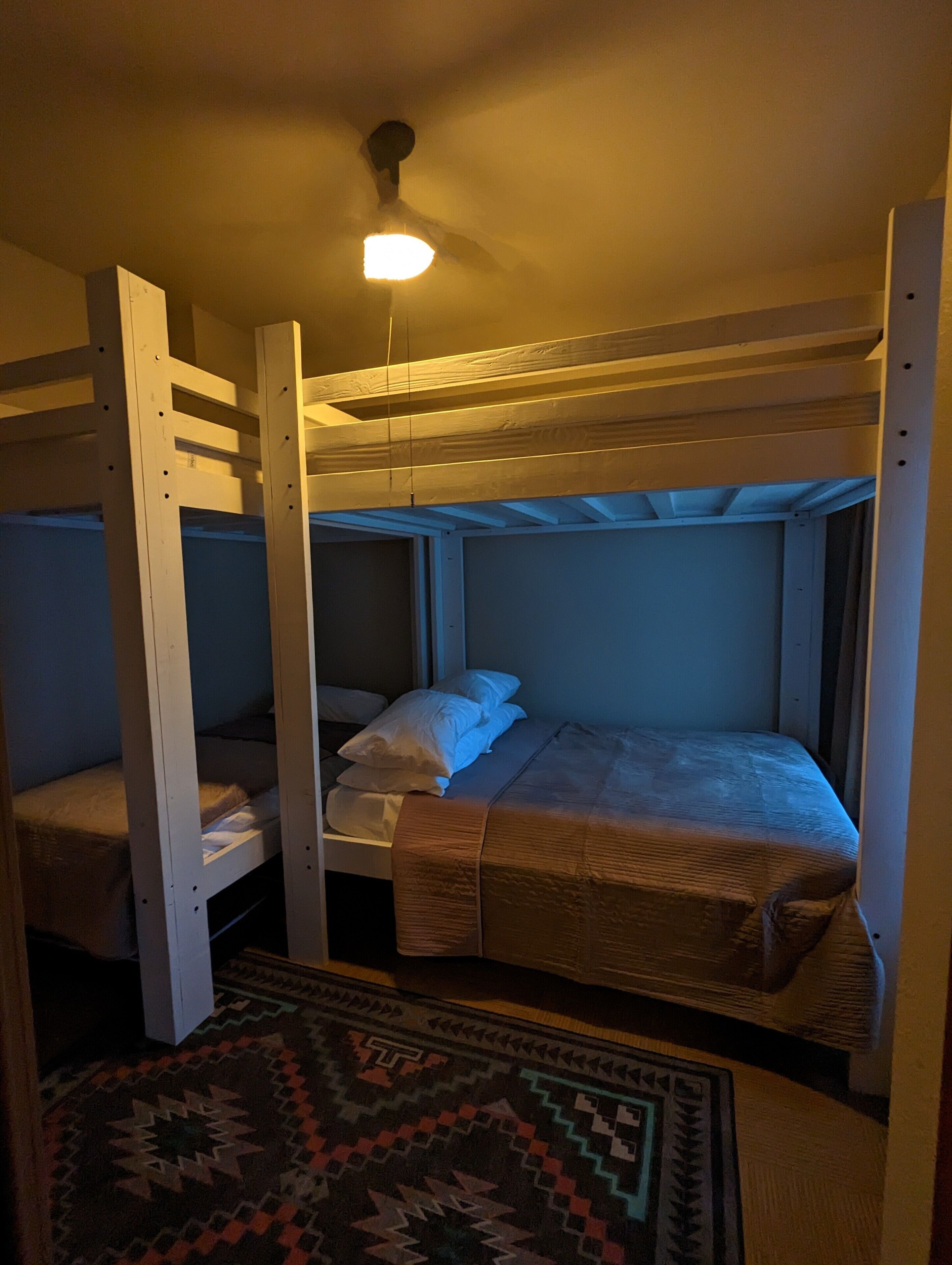 Een slaapkamer met een stapelbed, een plafondventilator, een kamerbreed tapijt met een patroon en een raam met gordijnen.