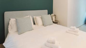 A neatly made bed with pillows, a bedside table with a lamp, and a towel stack.
