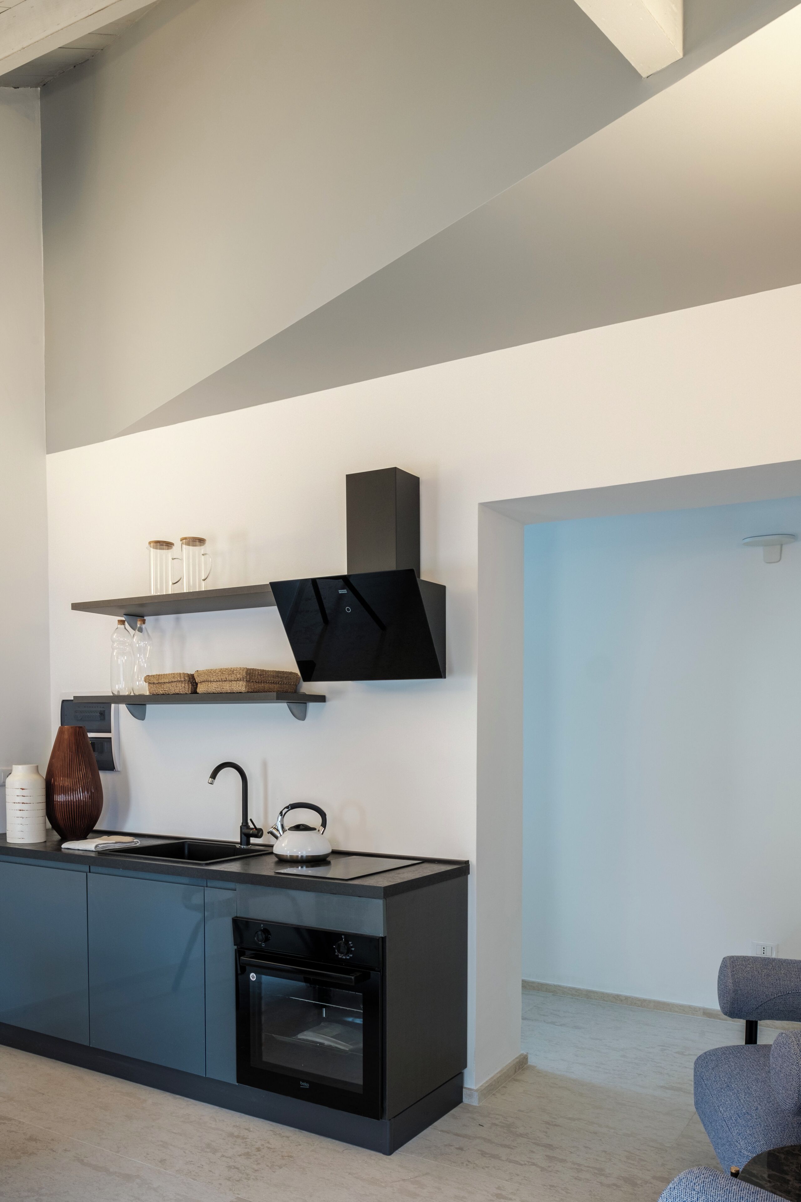 A modern kitchen with a built-in oven, a black countertop, and a wall-mounted shelf with kitchenware.