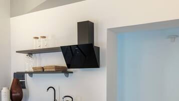 A modern kitchen with a built-in oven, a black countertop, and a wall-mounted shelf with kitchenware.