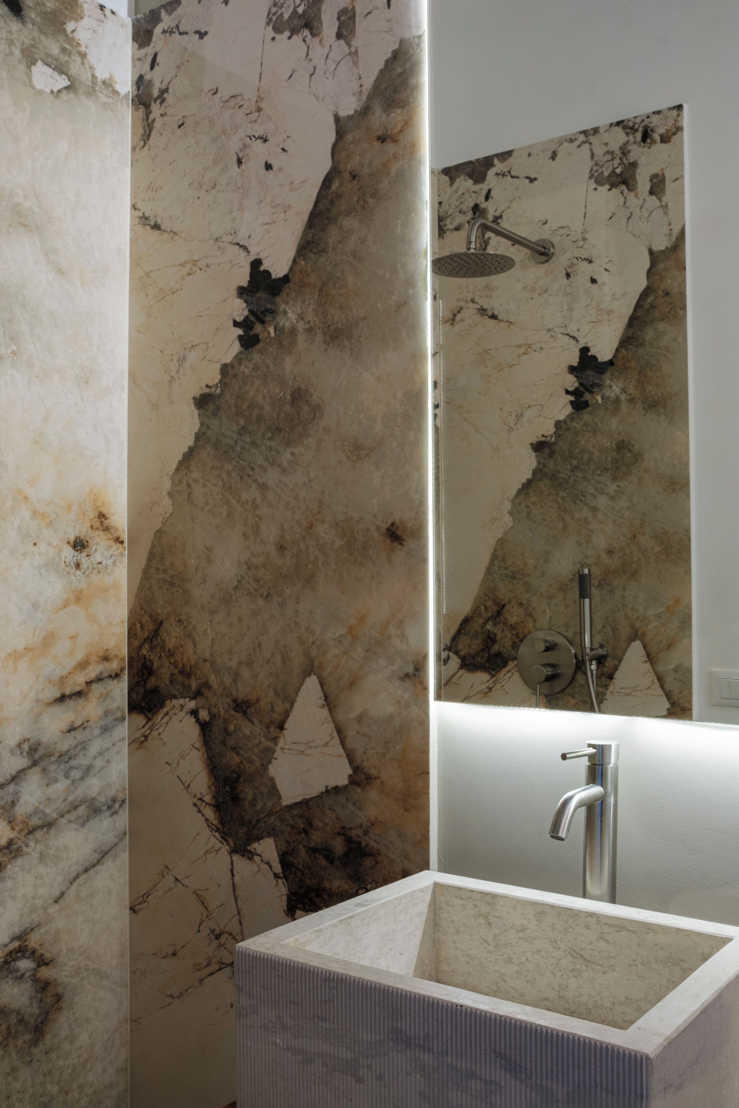 A bathroom with a marble wall, a sink, and a shower.