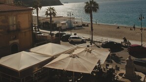 A coastal town with a beach, palm trees, and buildings with outdoor seating. - La Balza di Scilla (Scilla)