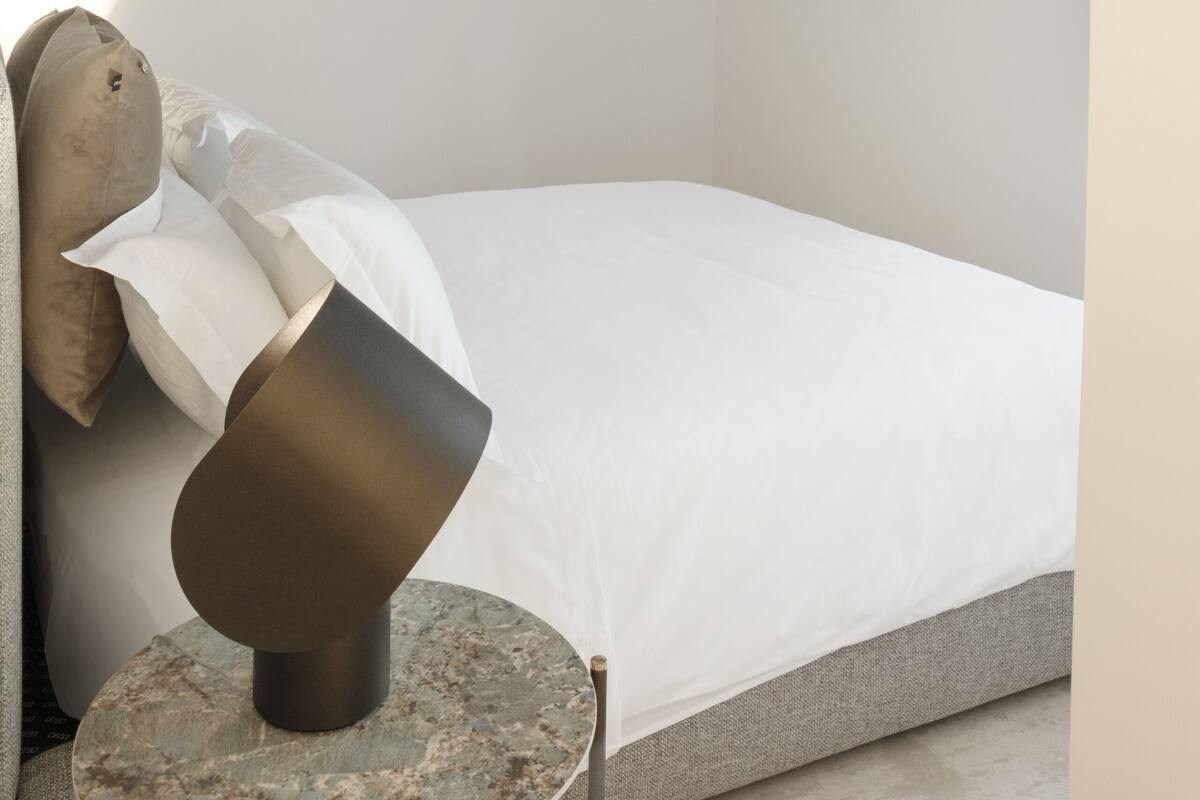 A bedroom with a bed, a round table with a lamp, and a TV mounted on the wall.