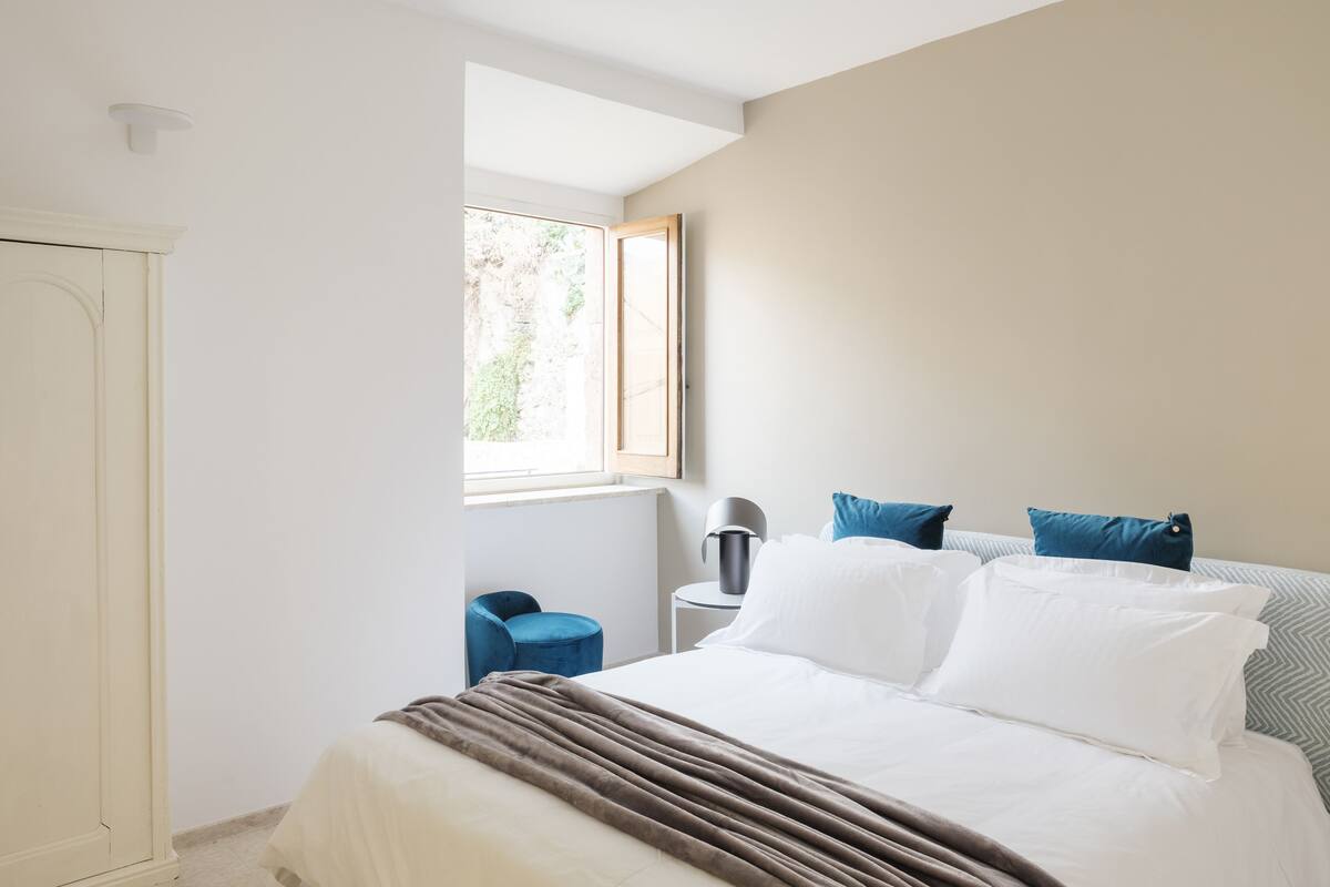 A bedroom with a bed, a window, a chair, and a lamp.