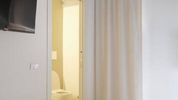 Une chambre à coucher avec un lit, un téléviseur fixé au mur et une salle de bain visible à travers une porte ouverte.