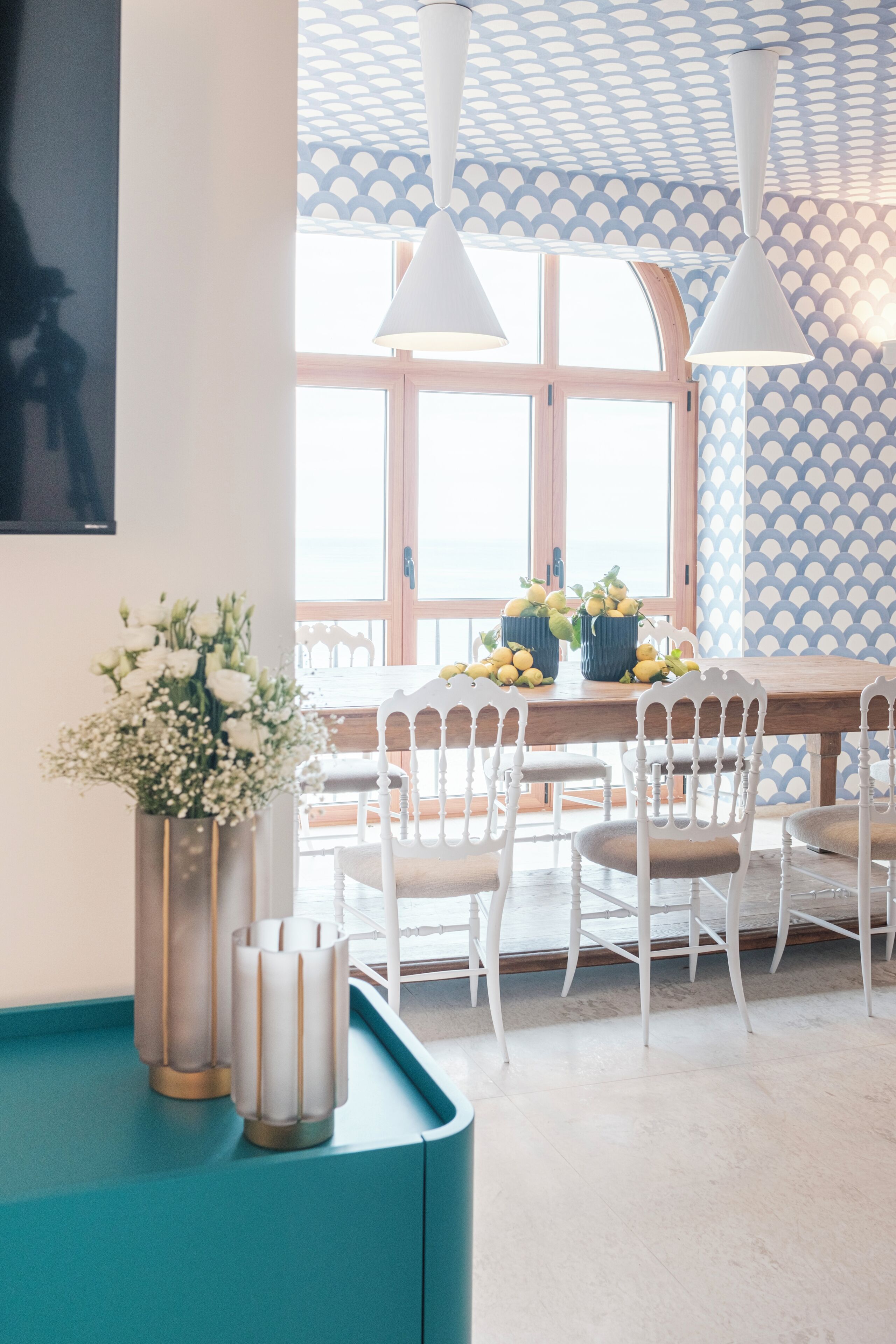 A dining area with a wooden table, white chairs, and a vase of flowers.